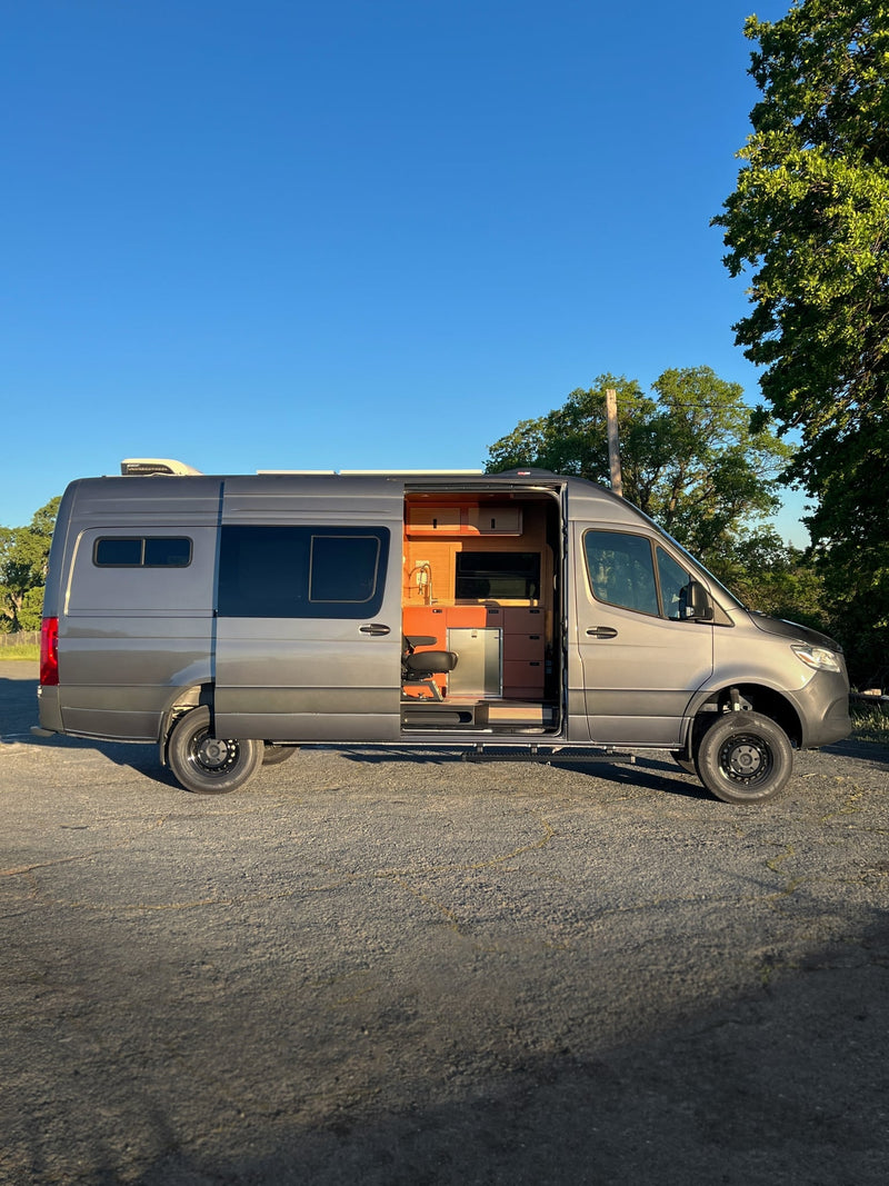 A sleek gray rv rental camper van is parked outdoors with its side door open — photo 1