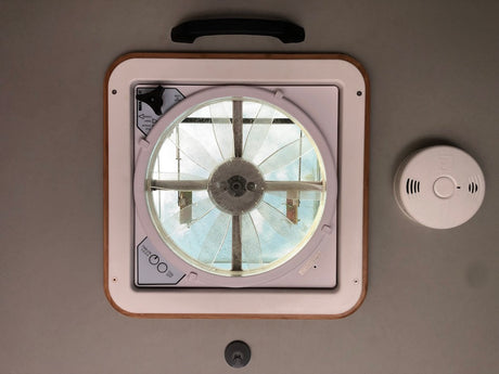 Ceiling of an rv rental showing a large vent fan for airflow, a smoke/CO detector, and small pull handle.