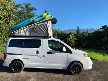 White pop-top camper van with surfboards on roof, perfect for an RV rental adventure with mountain views.
