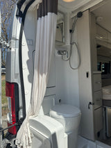 Compact rv rental wet bath with a shower, toilet, privacy curtain, and mirror inside a camper van.