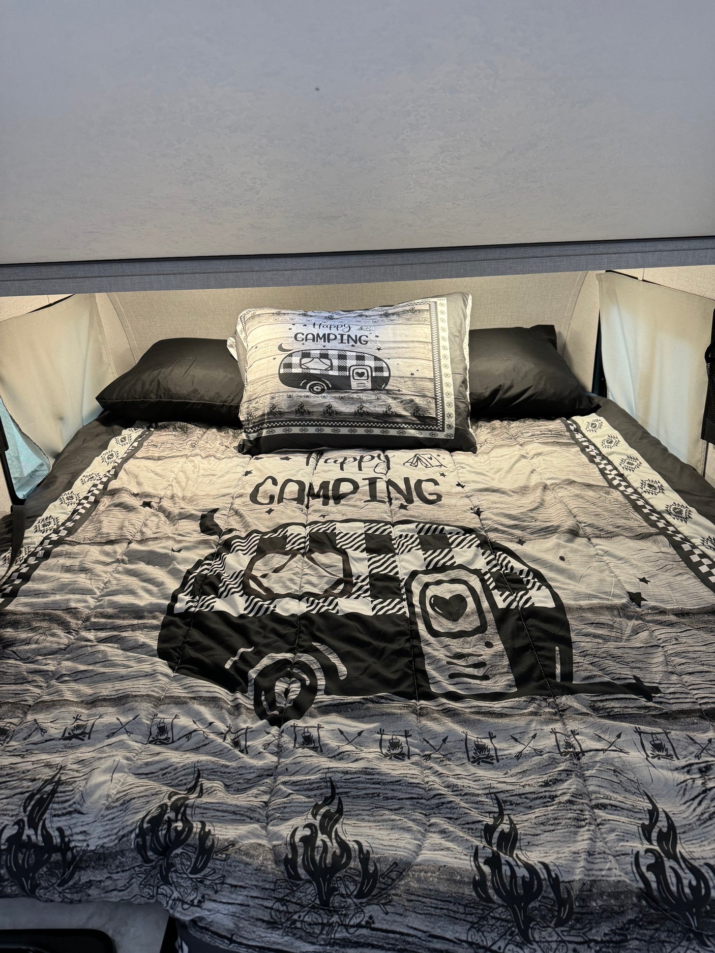 Cozy RV rental bed with "Happy Camping" comforter & pillow, featuring a black & white camper design.