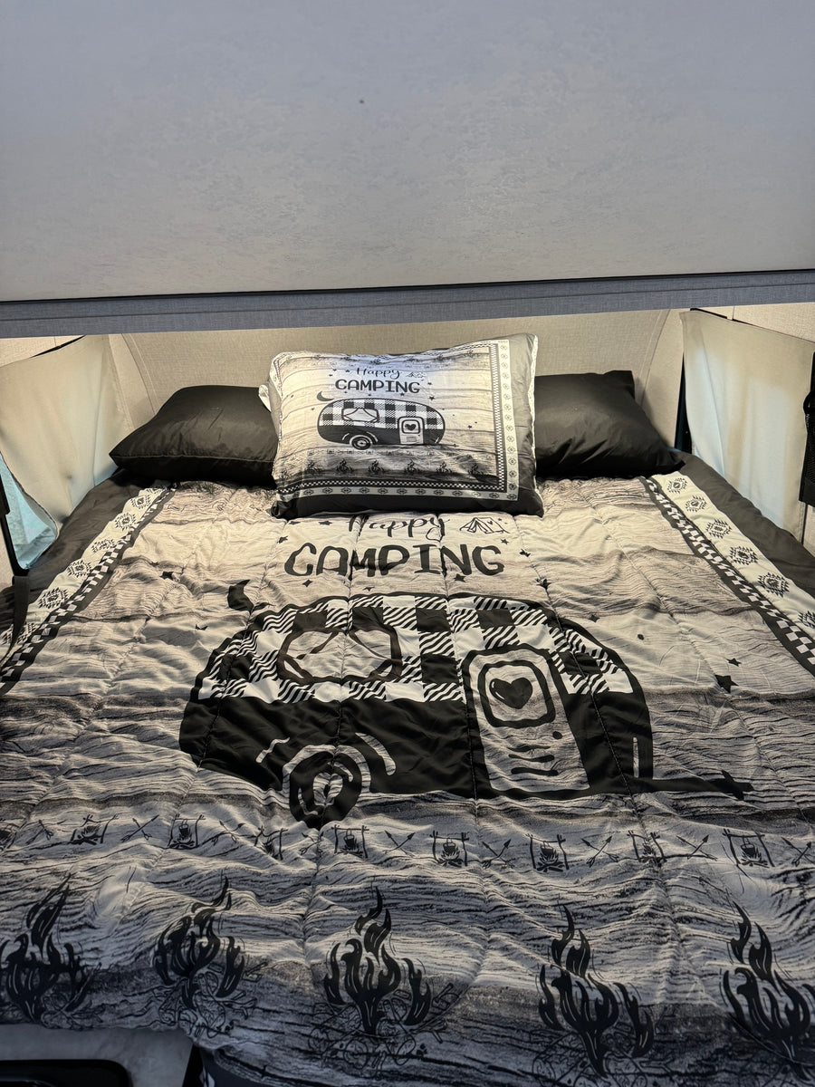 Cozy RV rental bed with "Happy Camping" comforter & pillow, featuring a black & white camper design.