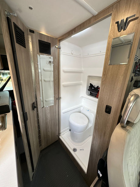 Compact RV rental wet bath interior, featuring a white toilet, shower, and wood-paneled folding door.
