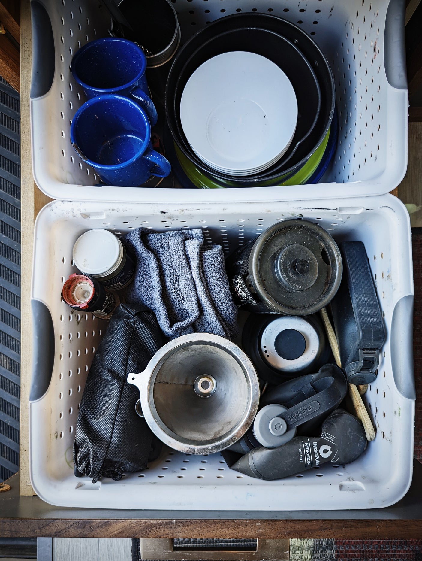 Two bins packed with RV rental camping supplies: blue mugs, nested cookware, and essential gear for your adventure.