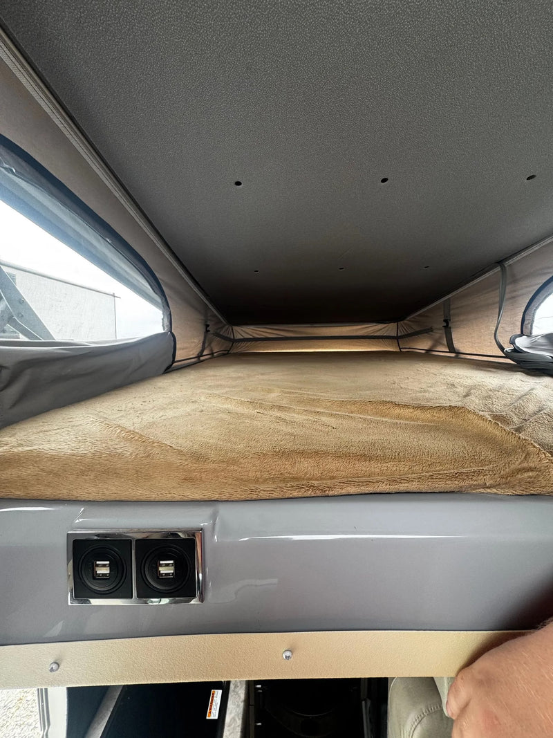 Looking up into an RV rental pop-top bed area with a plush blanket, side windows, and built-in USB ports. — photo 11