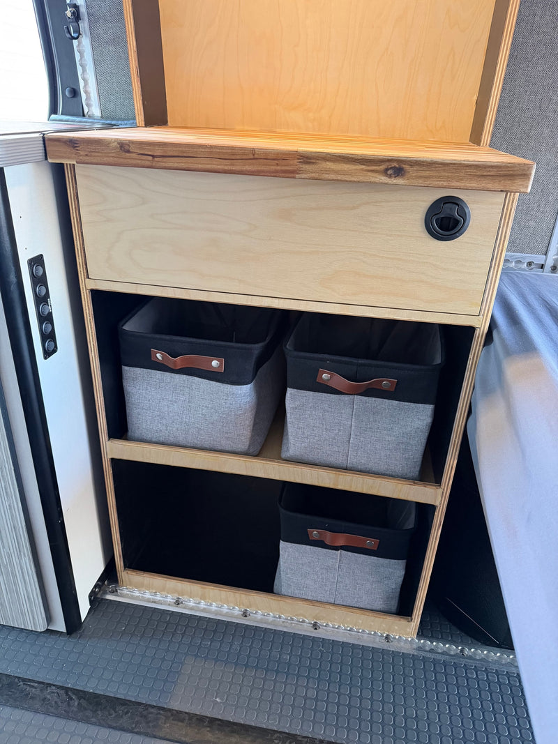 RV rental camper van interior featuring wooden storage cabinet, drawer, and fabric bins for organized living space, with control switches. — photo 13
