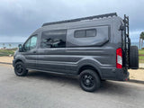 Sleek grey adventure van with roof rack, ladder, and rear tire, parked by the ocean. Perfect RV rental for van life travel.