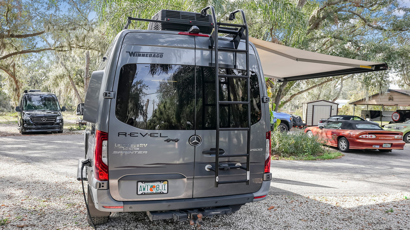 Experience adventure with this gray Winnebago Revel 4x4 Sprinter camper van rental, parked outdoors with another van nearby.