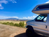 Silver RV rental van on a dirt road. Enjoy sweeping views of vast plains and distant mountains under a clear blue sky.