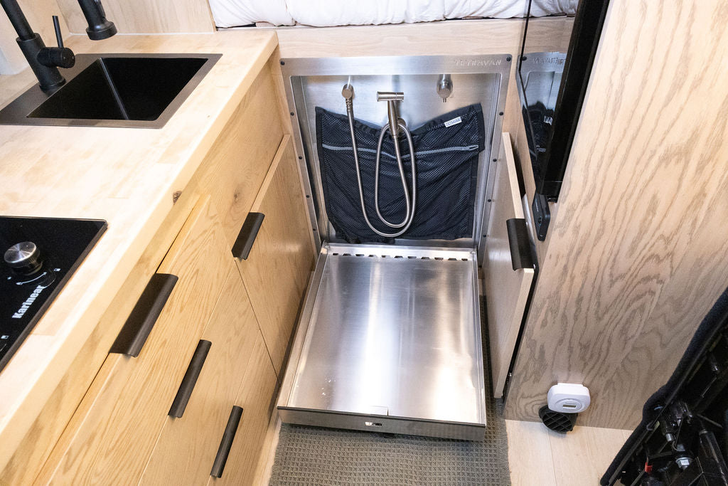 Compact RV rental interior: integrated kitchen with stovetop & sink, plus a clever pull-out shower system for efficient van life.