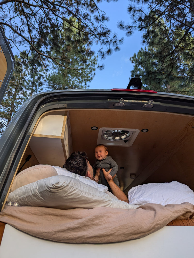 An RV rental provides a cozy space for a father and his baby to bond, looking out at pine trees from the open rear doors. — photo 18