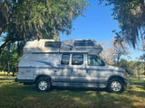 Silver Airstream 190 camper van, a perfect RV rental for exploring outdoors. Parked by a lake under mossy trees.