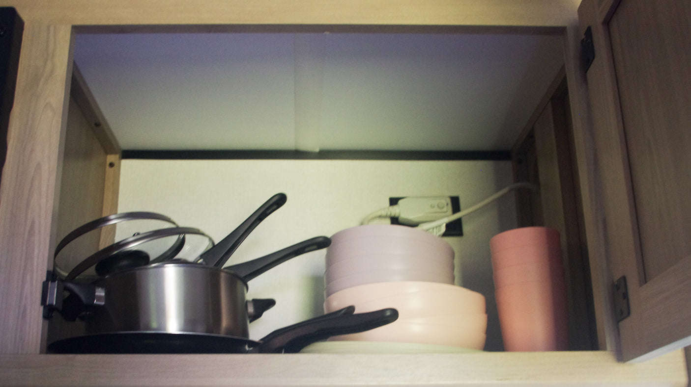RV rental kitchen: pots, pans, and durable dishes stored in a cabinet with an outlet.