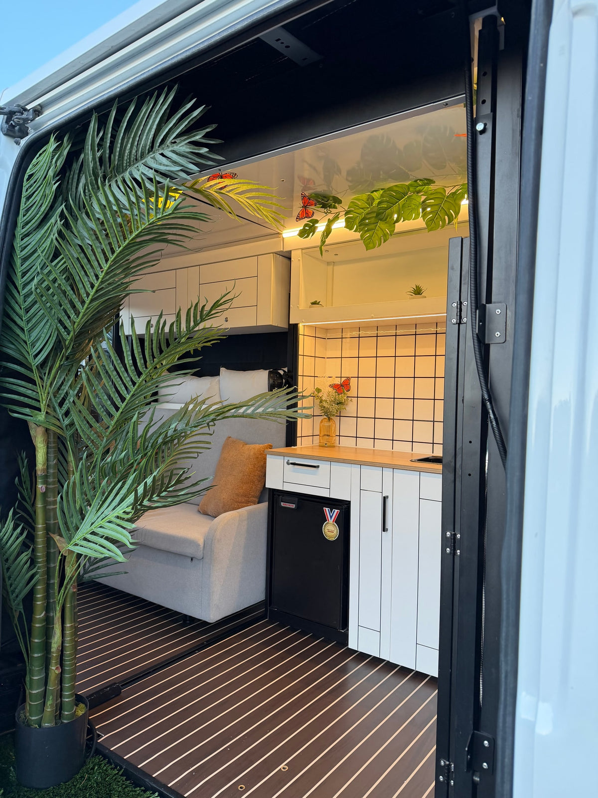Modern RV rental interior: a sleek kitchen, comfy sofa, and lush tropical decor, seen from the open door. — photo 15