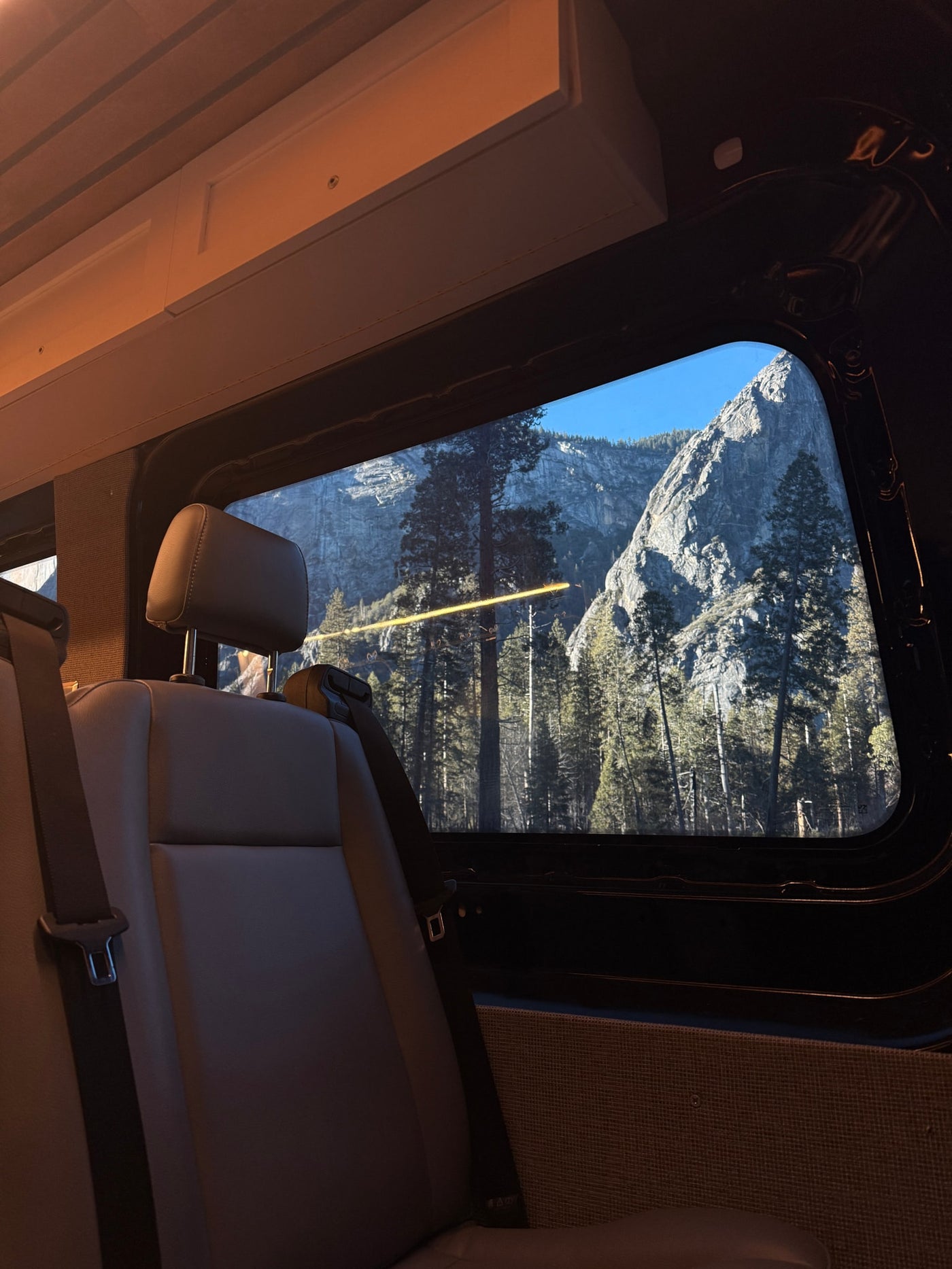 Inside this RV rental, rear seats offer a stunning window view of towering grey mountains, evergreen trees, and clear blue sky. — photo 12