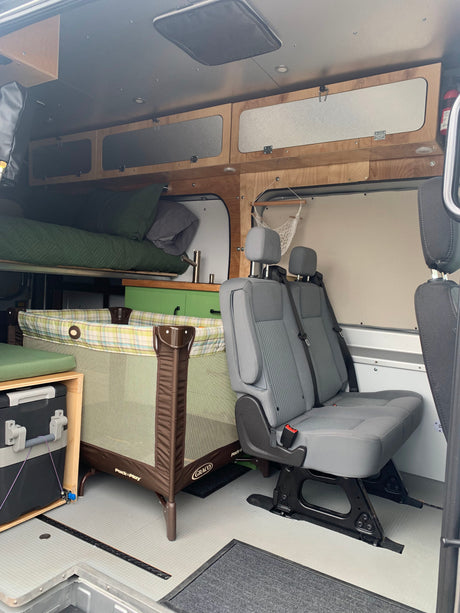 Spacious RV rental interior: a child's portable crib, passenger seats, and an elevated bed are visible, ideal for family trips.