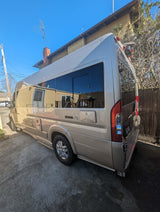 A champagne-colored Roadtrek Zion camper van (RV rental) is parked on a bright concrete driveway.