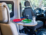 Cozy RV rental dining setup: Colorful plates, bowl, and mugs on a small table between seats. Perfect for campervan road trip meals.