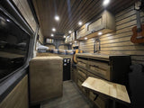 This RV rental showcases a warm wood-paneled interior with a built-in kitchen, bed, and cozy lighting.