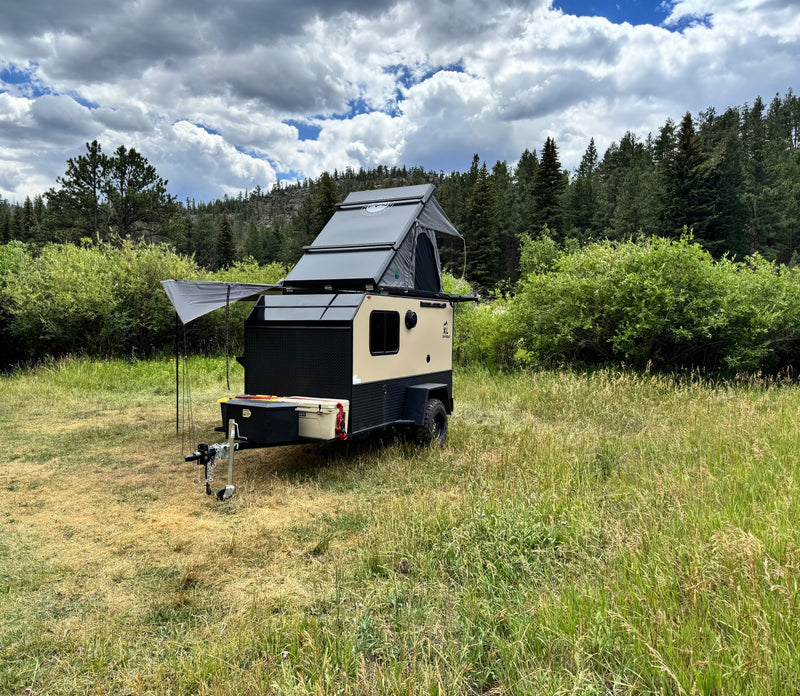 Rugged off-road camper RV rental with rooftop tent, set in a scenic field with forests and cloudy sky. Perfect for adventure. — photo 1
