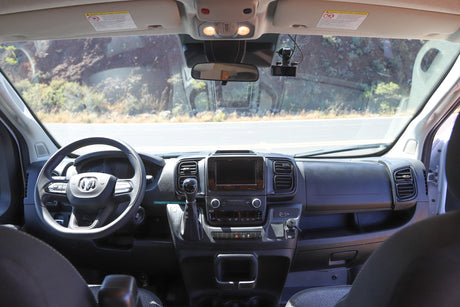 Interior of an RV rental van showing the dashboard, steering wheel, and windshield view of the road.