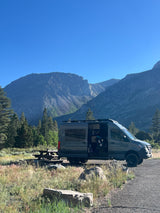 Experience nature with this RV rental camper van at a scenic mountain campsite. Picnic table ready for adventures.