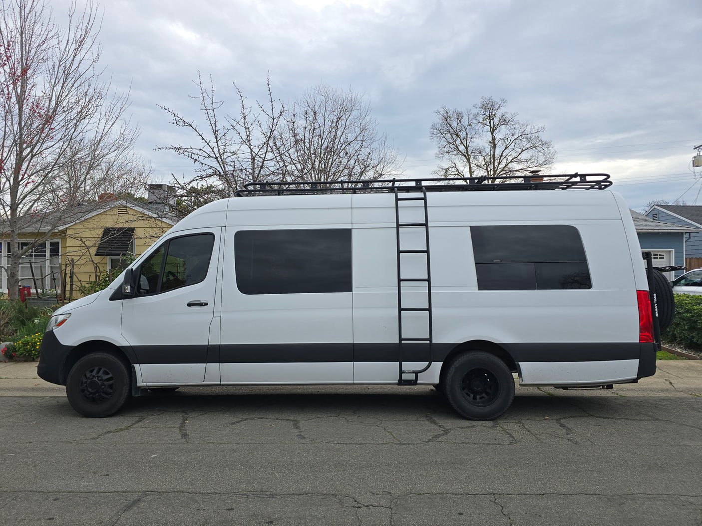 White Mercedes Sprinter camper van for RV rental, featuring a roof rack and side ladder.