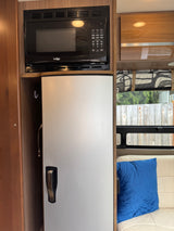 Compact rv rental kitchen: a High Pointe microwave over a silver refrigerator within wood cabinetry.