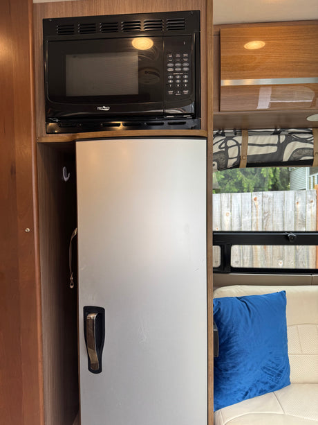 Compact rv rental kitchen: a High Pointe microwave over a silver refrigerator within wood cabinetry.