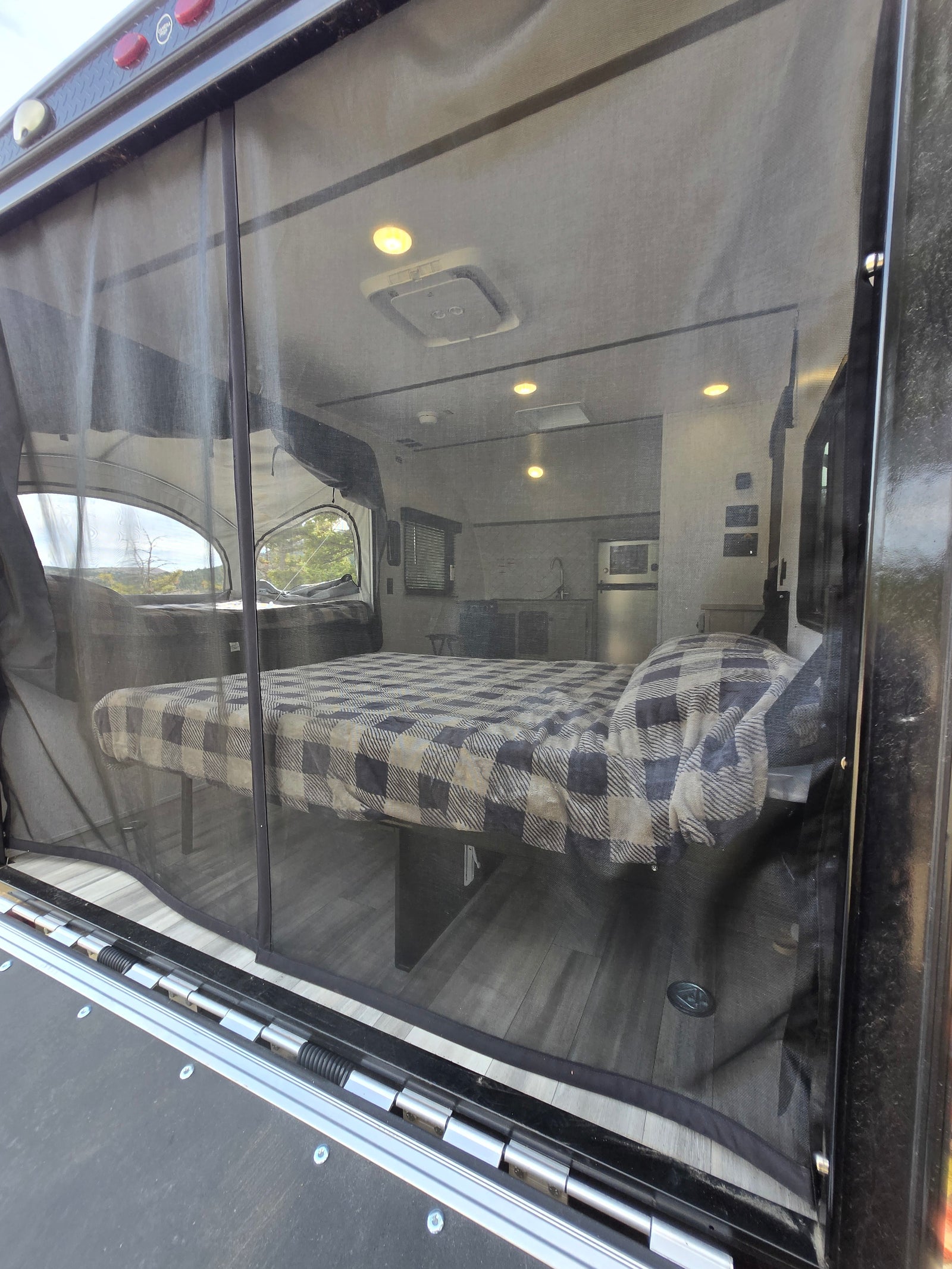 RV rental interior visible through screen: bed, kitchen, and scenic pop-out window. Enjoy comfortable camping.