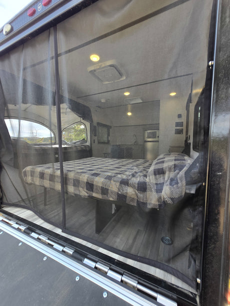 RV rental interior visible through screen: bed, kitchen, and scenic pop-out window. Enjoy comfortable camping.