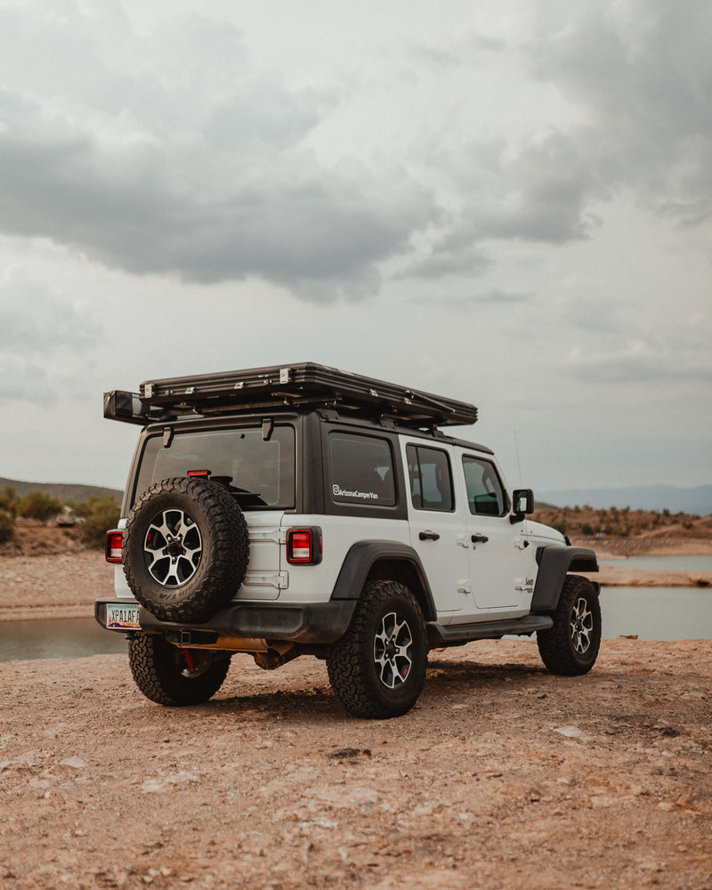 White Jeep Wrangler with rooftop tent, ideal for your next off-road RV rental adventure. Parked lakeside under cloudy skies. — photo 11