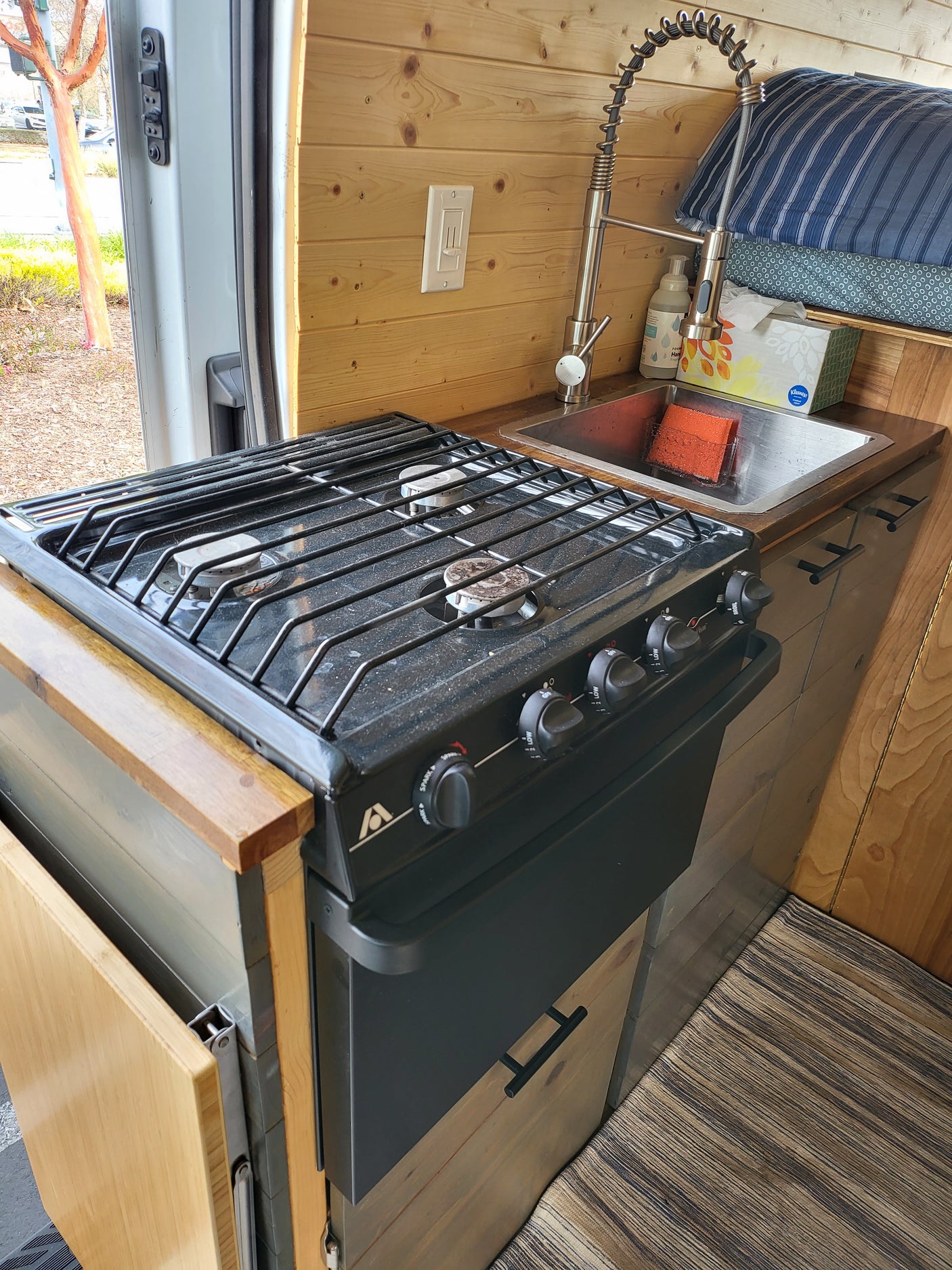 Functional RV rental interior: wood-paneled kitchen with a flexible faucet, sink, and gas stove/oven.