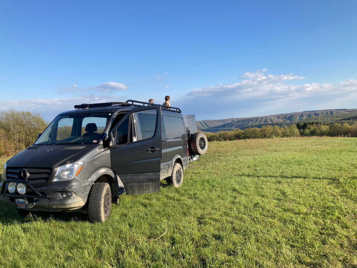 A grey camper van (RV rental) in a green field under a vast blue sky. Two children watch the distant mountains from its roof. Perfect for family adventures. — photo 17