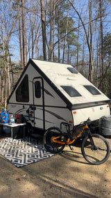 Enjoying a Flagstaff A-frame camper and mountain bike in a wooded campsite. Ideal for your next rv rental camping trip!