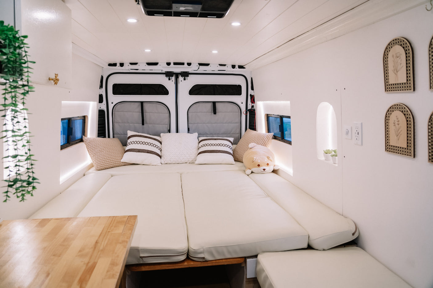 Interior of a modern rv rental camper van, featuring a spacious, cozy bed with cream cushions and stylish white decor.
