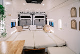 Interior of a modern rv rental camper van, featuring a spacious, cozy bed with cream cushions and stylish white decor.
