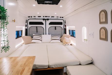 Interior of a modern rv rental camper van, featuring a spacious, cozy bed with cream cushions and stylish white decor.