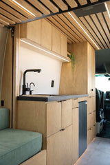 Modern RV rental galley with light wood cabinetry, black sink, fridge, and stylish LED lighting.