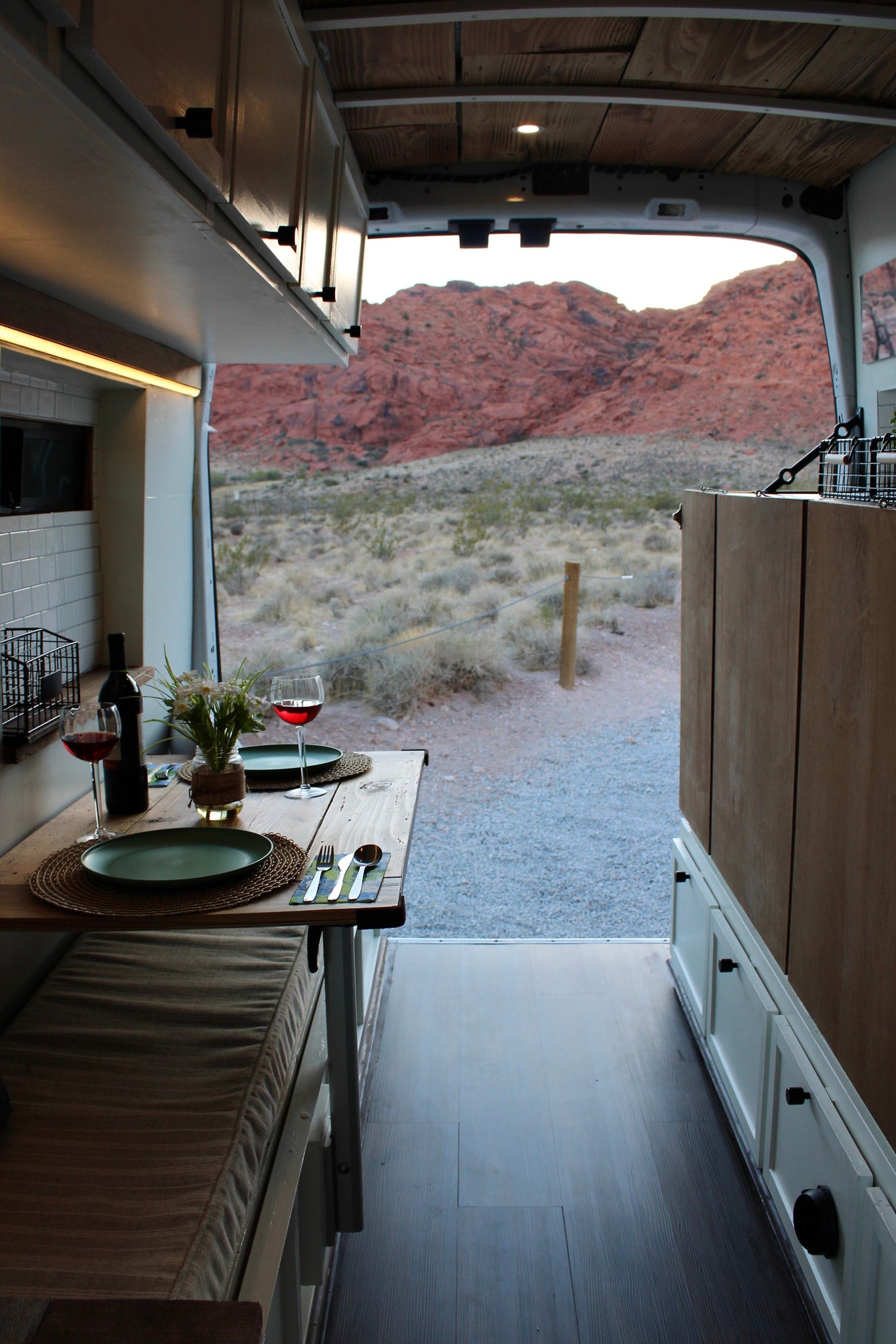 A cozy RV rental camper van interior with a dinner table set for two, overlooking red rock mountains at sunset. — photo 8