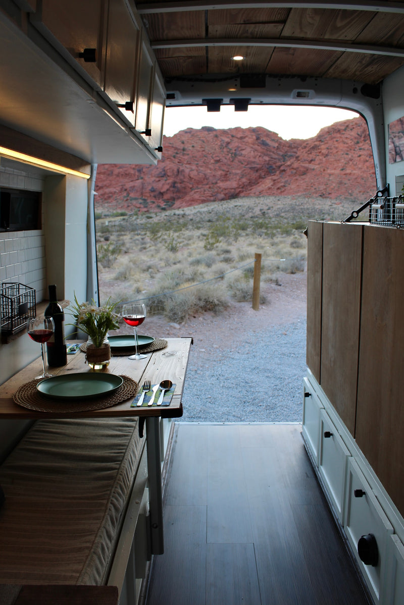 A cozy RV rental camper van interior with a dinner table set for two, overlooking red rock mountains at sunset. — photo 8