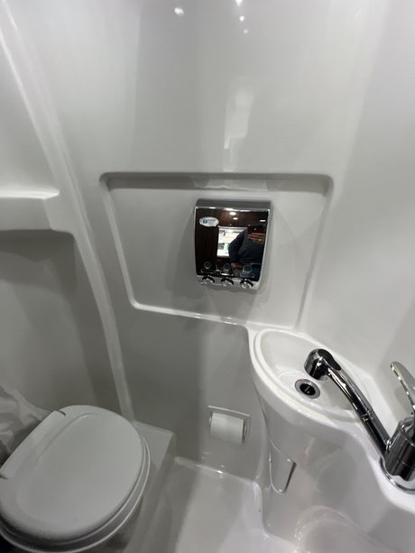 Compact RV rental bathroom with white toilet, sink, and wall-mounted dispenser. Efficient use of space.