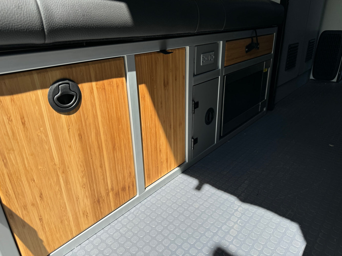Modern RV rental interior with custom bamboo cabinets, black latches, USB outlet, microwave, and textured gray flooring. — photo 12