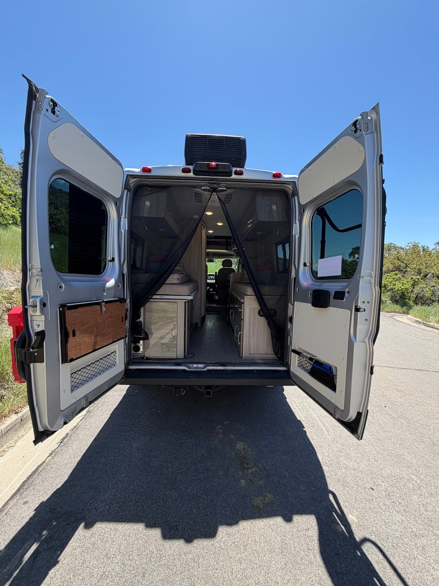 Inside an RV rental, rear doors open wide, revealing two beds, cabinets, and a kitchenette. Ideal for road trips and camping. — photo 11