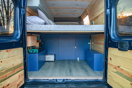 Inside this custom rv rental campervan, see the raised bed, blue storage, and wood accents.