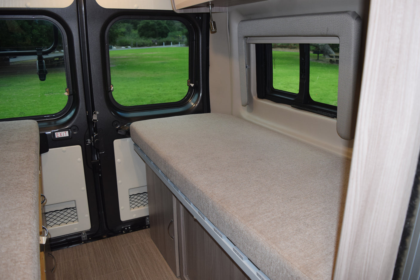 Comfortable RV rental camper van interior featuring twin beds, large windows with outdoor views, and under-bed storage.