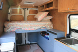This rv rental features a well-designed camper van interior with a comfy bed, kitchen sink, and ample storage.