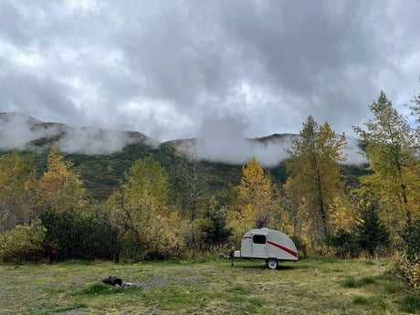 Teardrop RV rental among golden autumn trees, under misty mountain clouds. Scenic camping awaits!