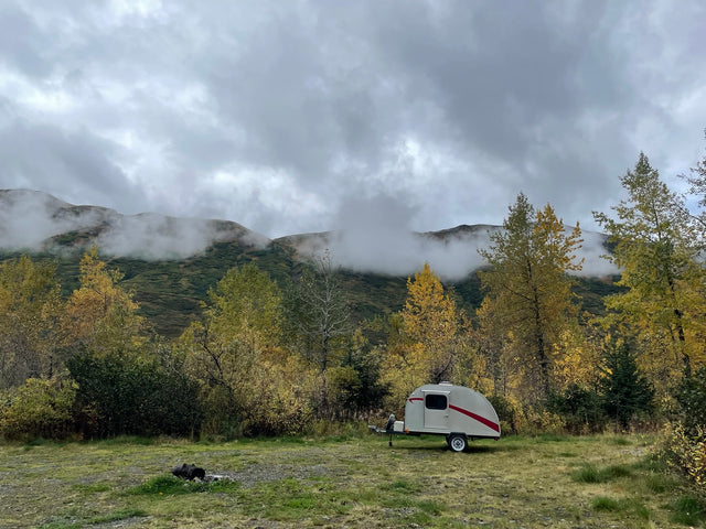 Teardrop RV rental among golden autumn trees, under misty mountain clouds. Scenic camping awaits!