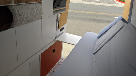 View inside an RV rental showing a clever interior with a fold-down table, bed, and custom storage.